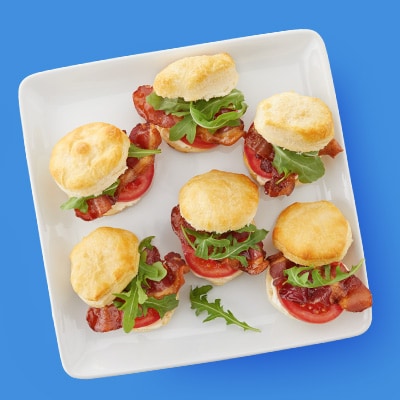 Mini BLT biscuit sandwiches served on a white plate with bacon, lettuce, and tomato – perfect appetizer or brunch idea.