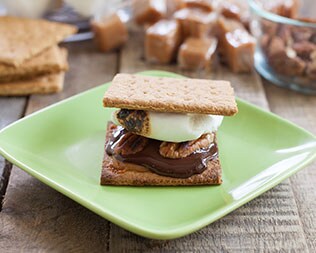 smore with pecans and melted chocolate on a green paper plate