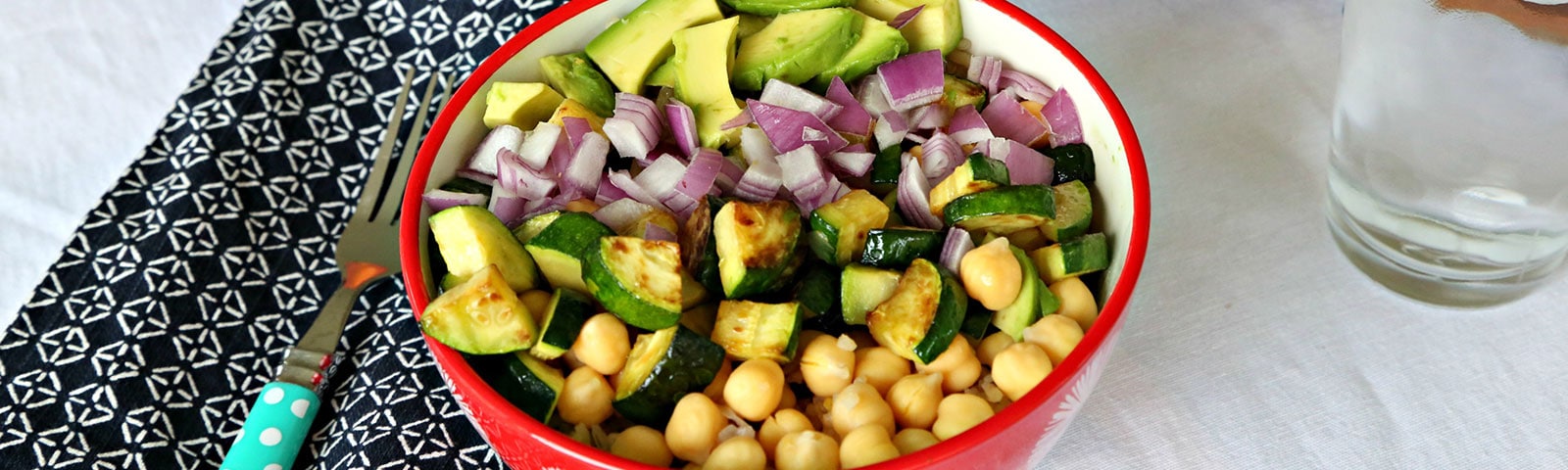 Colorful bowl filled with diced red onion, sliced avocado, sliced roasted zucchini and chickpeas