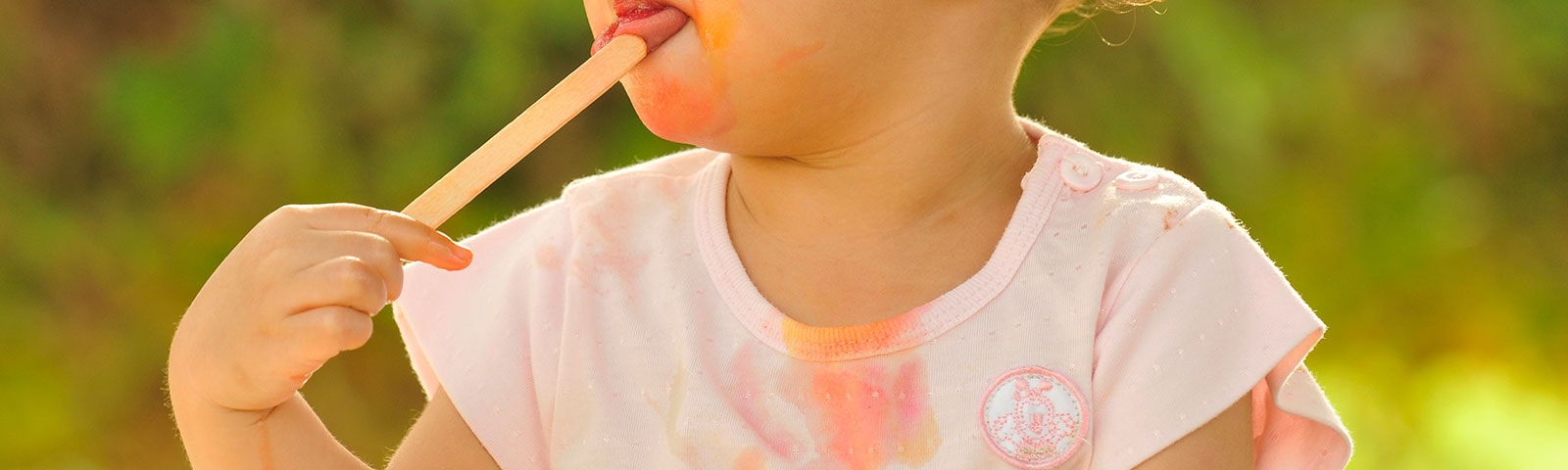 A young girl eating a melted popsicle with stains on her shirt