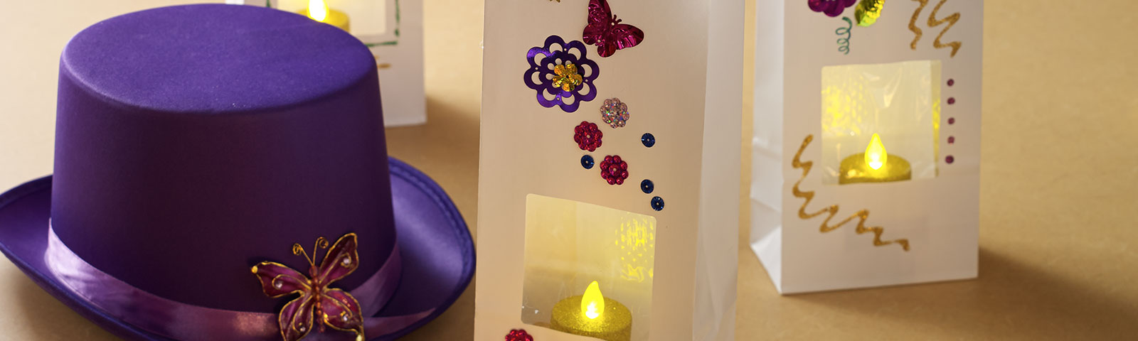 A purple top hat with a decorative brooch along with three white paper bags, decorated and filled with an LED candle