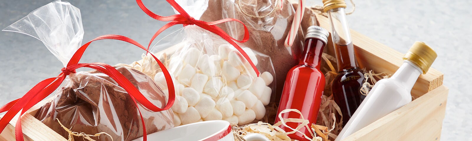 Wooden box filled with colorful mini liquor bottles, cocoa powder, and mini marshmallows 