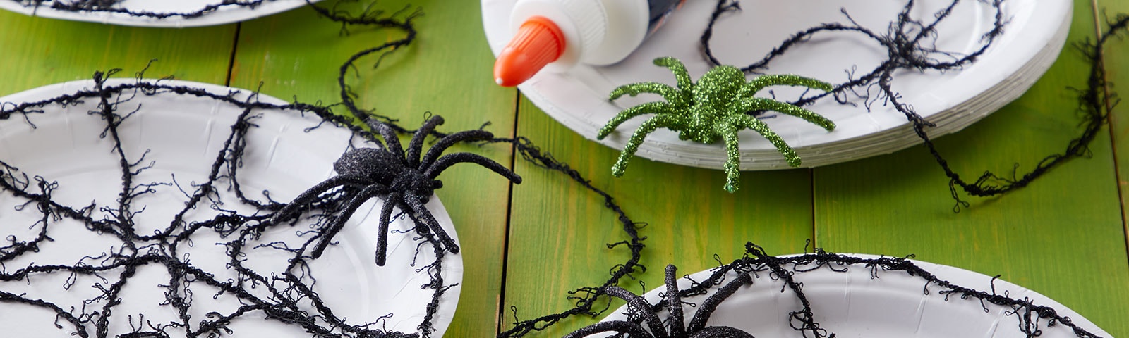 White paper plates with black yarn spiderwebs and black plastic spiders on top