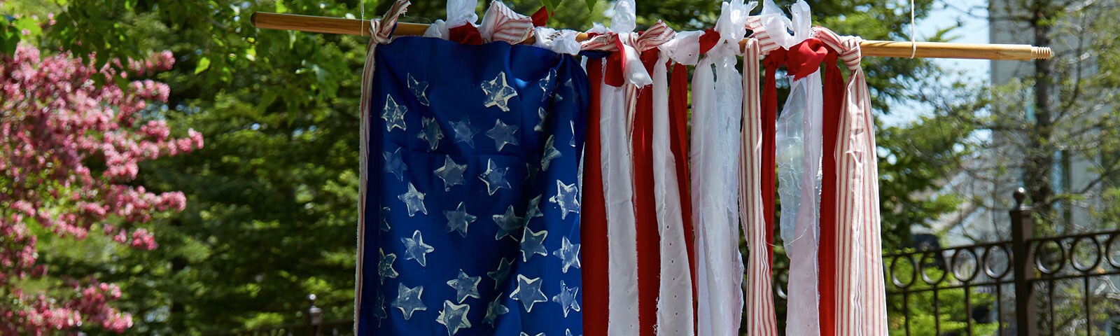A handmade American flag hanging outside created using long strips of red and white fabric that's tied to a hanging pole