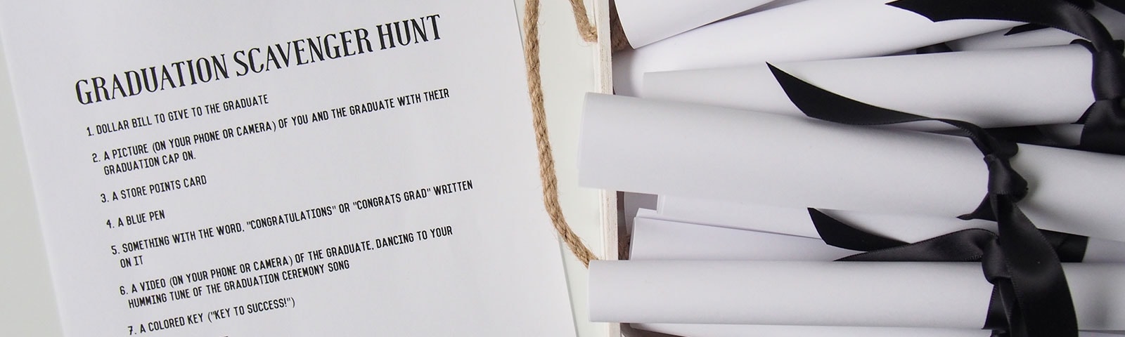 Rolls of white paper wrapped with black ribbon next to a Graduation Scavenger Hunt list