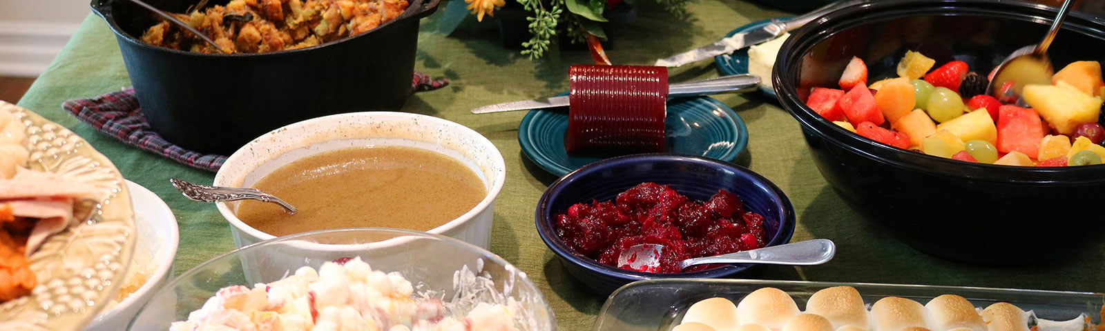 Thanksgiving potluck dishes like gravy and cranberry sauce on a table