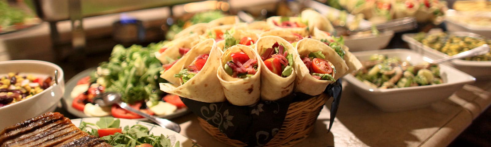 a bountiful feast of wraps, greens and pasta salads sit on a long countertop