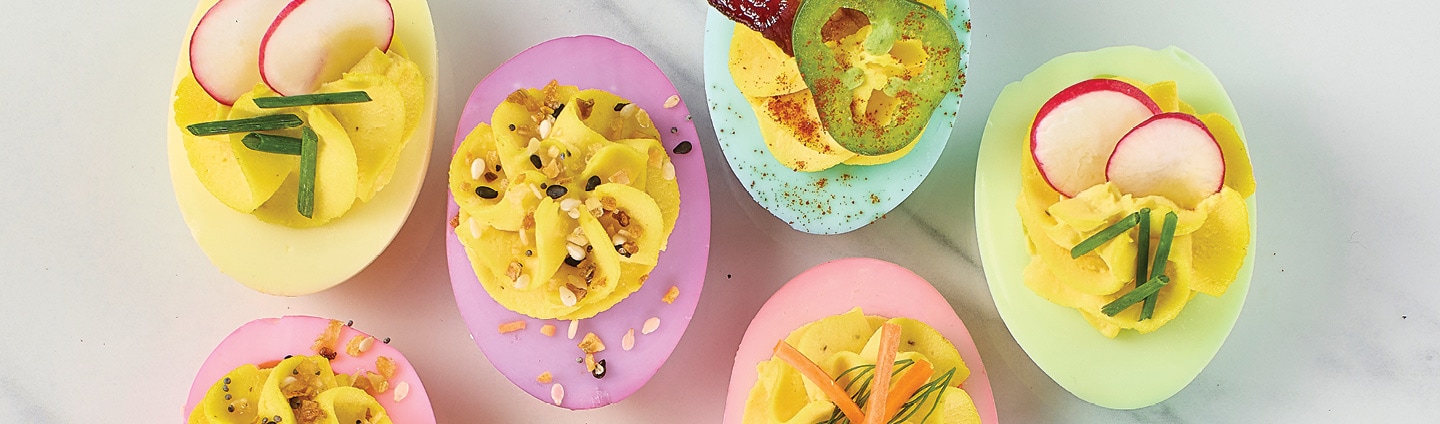 Assorted pastel deviled eggs with a variety of different toppings